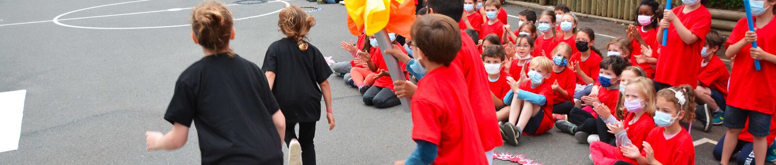 Des enfants habillés en rouge portent une flamme factice devant un public d'enfants